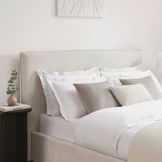 a bed with white sheets and pillows in a bedroom next to a painting on the wall