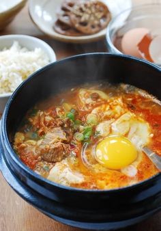 a bowl of soup with an egg in it and other dishes on the table behind it