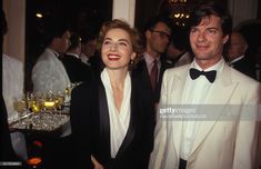 a man and woman standing next to each other at a formal event with wine glasses in front of them