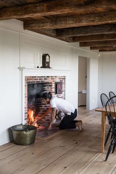 a man kneeling down next to a fire place in a room with wooden floors and white walls