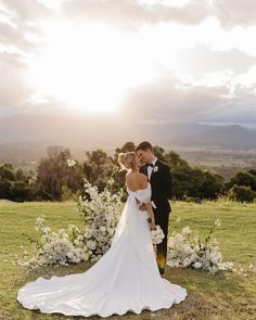 the bride and groom are standing in front of white flowers on their wedding day at sunset