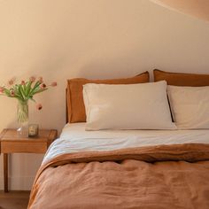 a bed with white and brown linens in a bedroom next to a wooden table