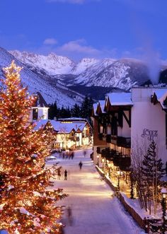 a christmas tree is lit up in the middle of a snowy town with mountains in the background