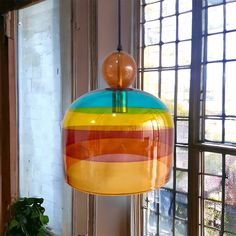 a multicolored lamp hanging from a ceiling in front of a window next to a potted plant