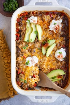 an enchilada casserole in a white dish with a wooden spoon