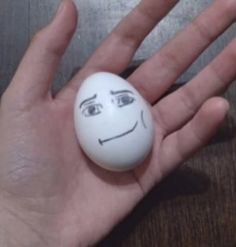 a hand holding an egg with a face drawn on it