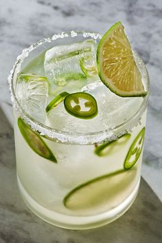 a close up of a drink in a glass with lime and an olive slice on the rim