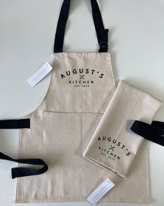 two aprons with tags on them are sitting next to each other, and one has a tag that says august's kitchen