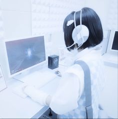 a woman wearing headphones sitting at a desk with a computer monitor and keyboard in front of her