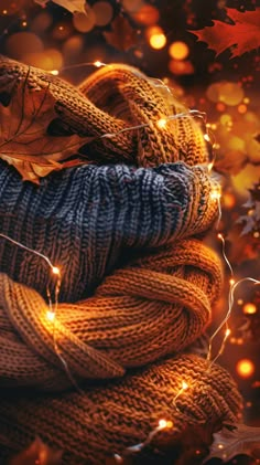 a pile of knitted blankets and lights in front of fall leaves on the ground