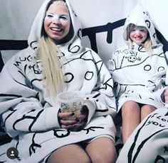 two women sitting on a couch wearing matching outfits and holding mugs in their hands