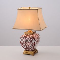 a red and white vase sitting on top of a table next to a lamp