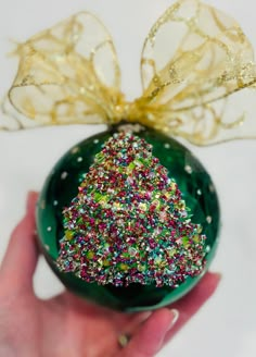 a hand holding a green ornament with a christmas tree on it's side