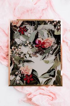 flowers and greenery are arranged in a square frame on a pink background with gold trim