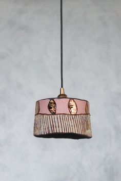 a pink and white lamp hanging from a black cord with two faces on the lampshade