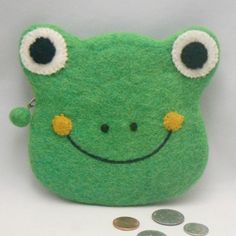 a green frog coin purse sitting on top of a white table next to some coins