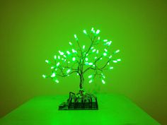 a small tree is lit up with green lights on the top and bottom branches, in front of a dark green background