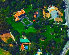 an aerial view of a large house in the middle of some trees and grass with a road running through it