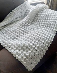 a white crocheted blanket sitting on top of a couch next to a window