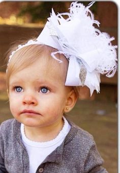 a baby girl wearing a white headband with feathers on it's head and looking at the camera