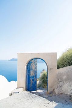 an open blue door on the side of a white building with water in the background