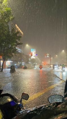 a city street at night in the rain with cars and motorcycles parked on the side