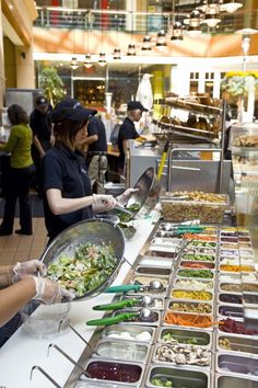 people are serving themselves food at a buffet table in a mall or restaurant with many different foods on it