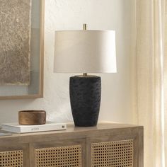 a lamp is sitting on top of a wooden cabinet in front of a painting and books