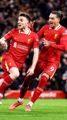 two soccer players in red uniforms are running on the field with their arms around each other