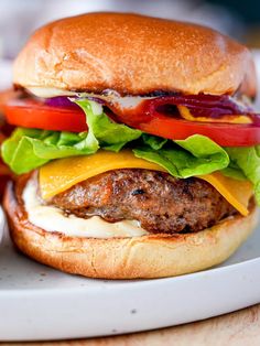 a hamburger with lettuce, tomato, and cheese on it sitting on a plate