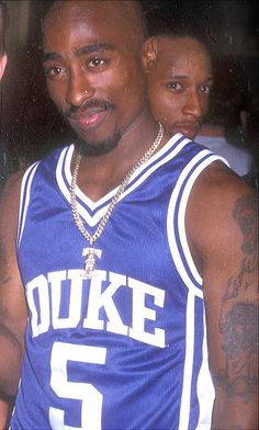 a man in a blue basketball uniform standing next to another man with tattoos on his arms