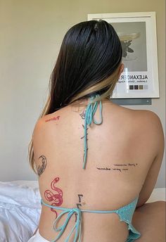 the back of a woman with tattoos on her upper and lower back, sitting on a bed