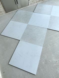 four white tiles laid out on the ground in front of a refrigerator and freezer