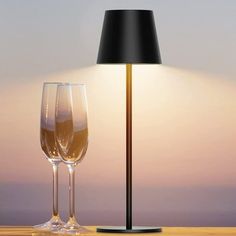 two wine glasses sitting on a table next to a lamp