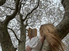 a woman sitting in a tree reading a book with her long hair blowing back over her shoulder