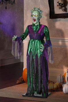 a creepy clown dressed in green and purple standing next to a wall with pumpkins on it