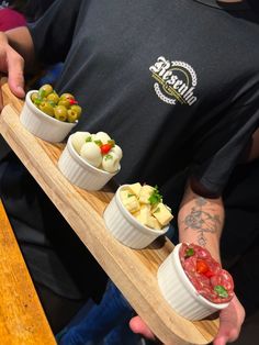 a man holding a tray with four small bowls filled with different types of food on it