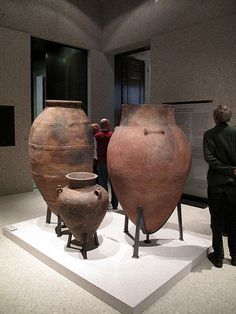 two large vases are on display in a museum with people looking at them and standing around