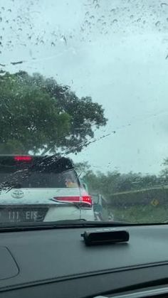 the rear view mirror of a car with rain on it and trees in the background