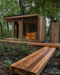 a wooden bench sitting in the middle of a forest next to a small building with an open door