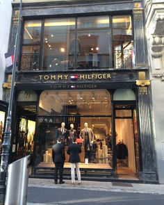 two people standing in front of a tommy hilfiger store on a city street