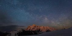 the night sky is filled with stars and clouds above snow covered mountains in the distance