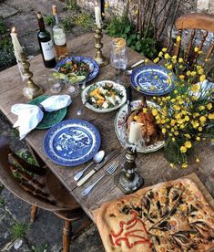 an outdoor table with plates and food on it, next to candles and flowers in vases