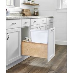 a kitchen with white cabinets and wood flooring is shown in this image, there is an open drawer on the left side of the cabinet