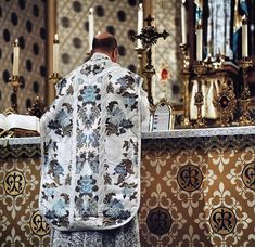 a priest standing at the alter in front of an ornate wallpapered church altar