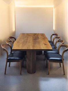 a wooden table surrounded by black leather chairs in a room with white walls and flooring