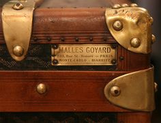 an old wooden suitcase with brass hardware and labels on the front, sitting in a display case