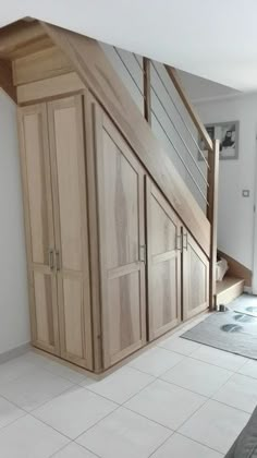 an empty room with wooden furniture and white tile flooring in front of a stair case