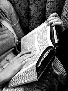 a woman sitting on a couch holding an open book in her lap and reading it