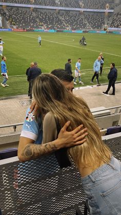 two people sitting on a bench at a soccer game, one is hugging the other